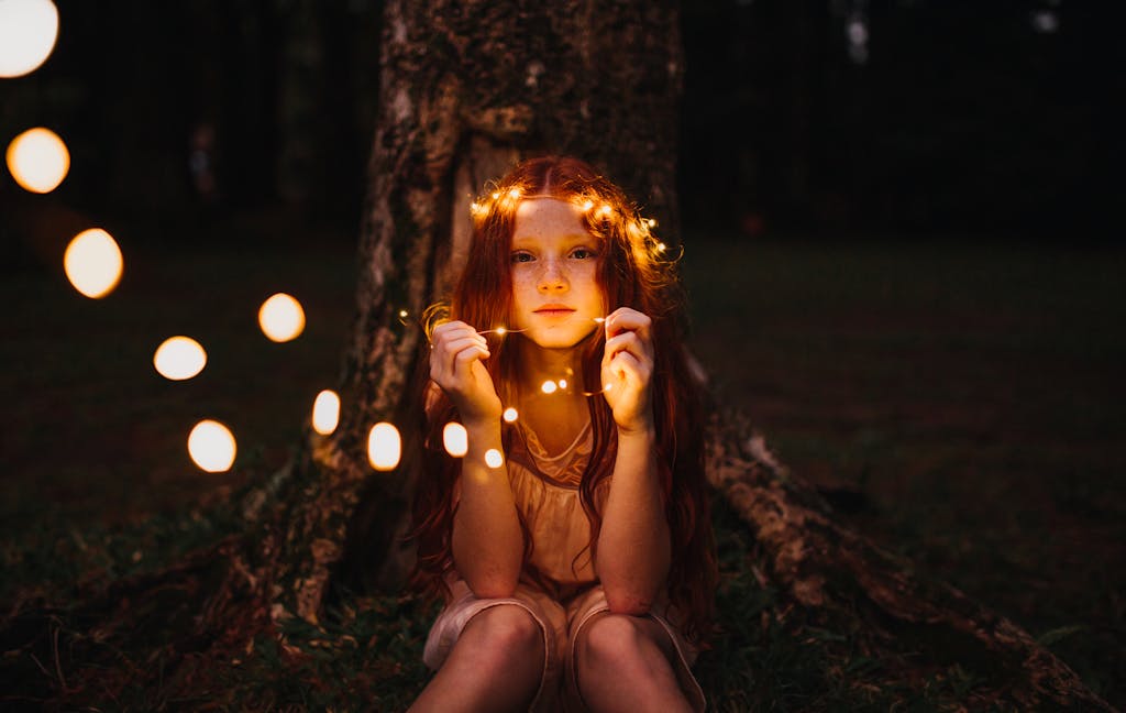 A young girl with fairy lights creates a magical evening mood outdoors.