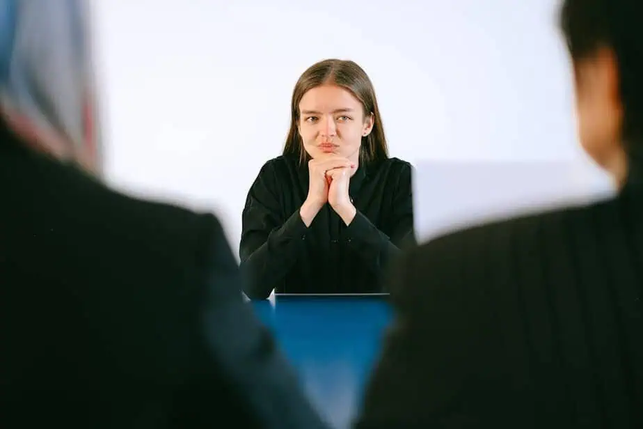 A woman in a job interview facing two people at an office table, focusing intently.
