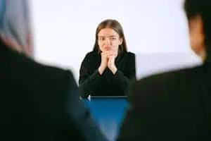 A woman in a job interview facing two people at an office table, focusing intently.