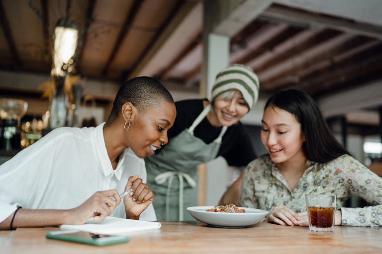 A joyful group of diverse women enjoying a meal together at a cozy café, engaging in cheerful conversation.