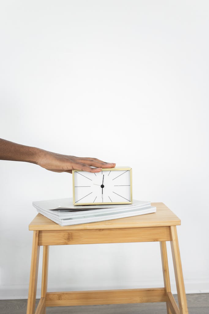 Photo by KATRIN  BOLOVTSOVA A minimalist clock being placed on a table, depicting time management and simplicity.