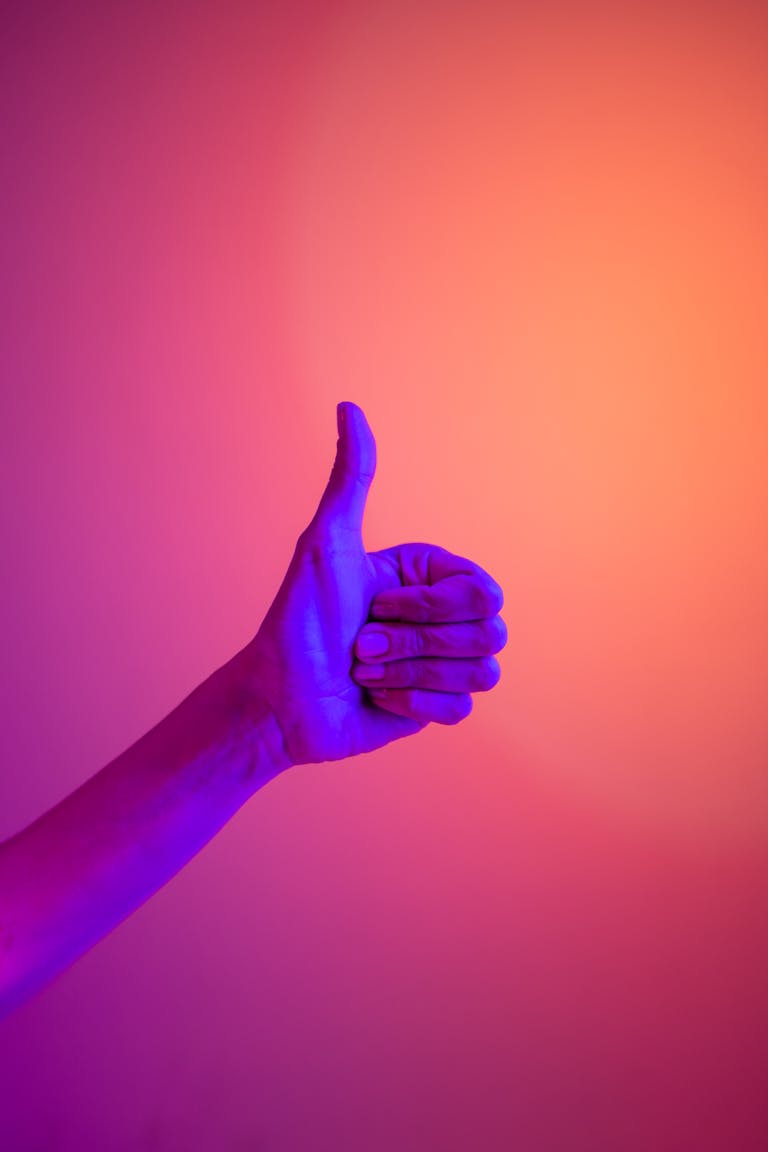 A neon-illuminated hand giving a thumbs up against a vibrant gradient background, symbolizing approval and positivity.