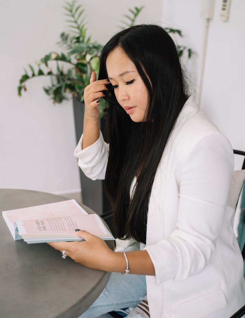 Photo by Anna Tarazevich Adult woman reading a book indoors, dressed in white, with a serene expression.