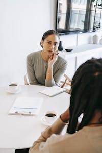 Serious ethnic female consultant listening to black male client problems while sitting at round table together in light psychology center