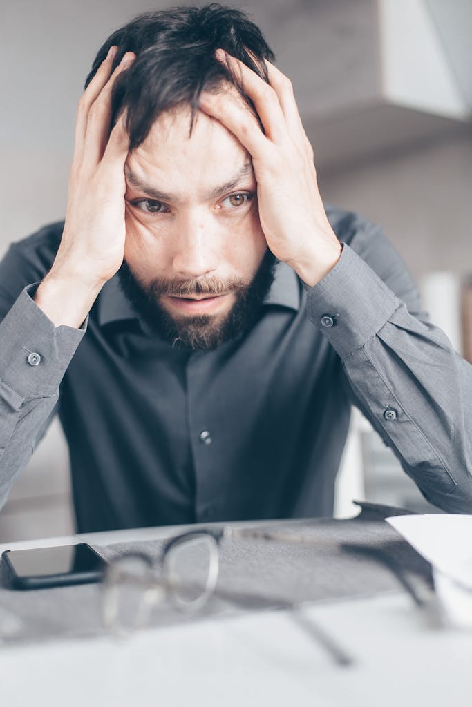 Man with hands on head looking stressed and frustrated indoors.