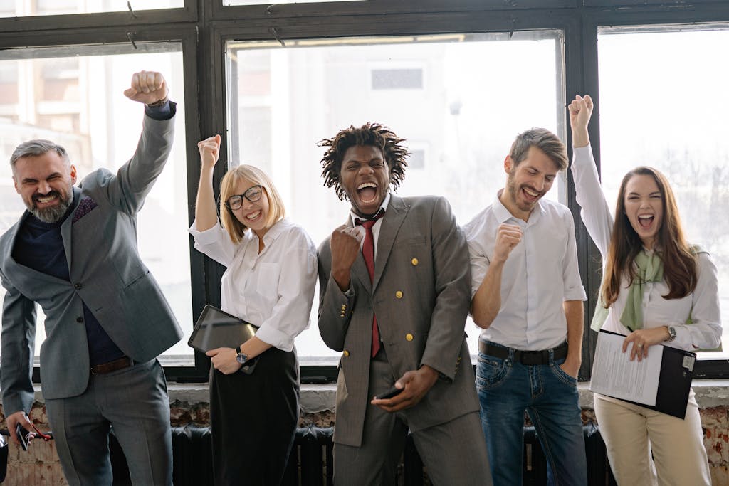 A joyful, diverse group of colleagues celebrating success indoors with cheerful expressions.