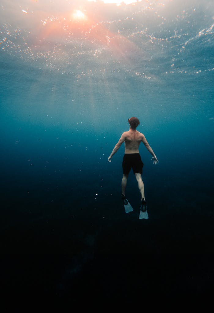 A man swimming underwater in the ocean, sunlight filtering through.