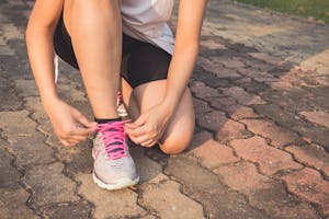 Adult woman tying pink laces on running shoes outdoors. Focuses on fitness and lifestyle.