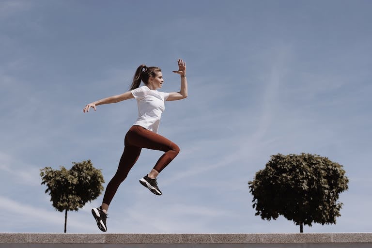 Athletic woman in action jump against a blue sky background. Captures fitness in motion.