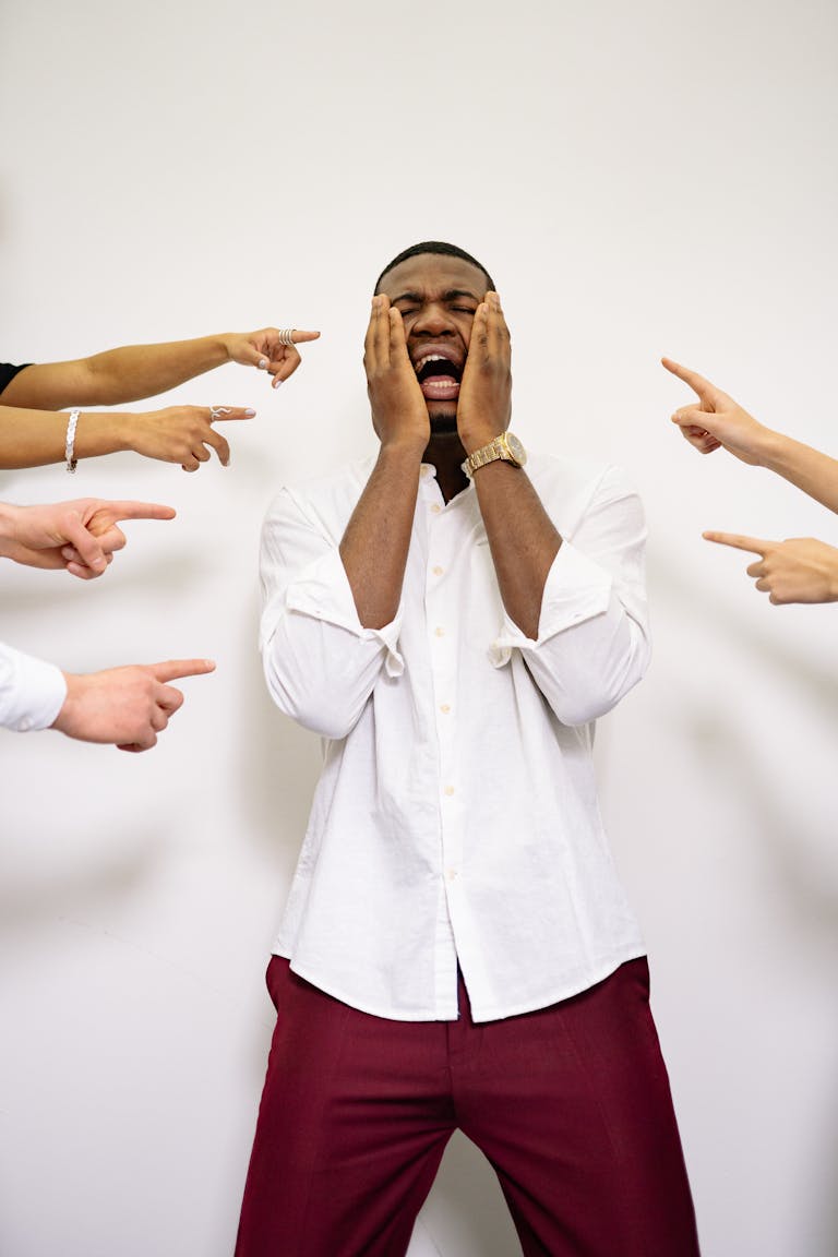 Businessman experiencing stress and despair as coworkers point fingers, highlighting workplace conflict.