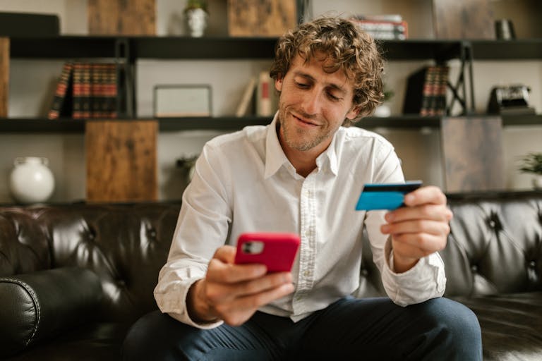 Caucasian man using smartphone and credit card for online shopping indoors.