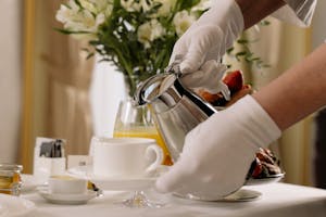 Elegant room service setting with coffee being poured by gloved hands in a hotel.