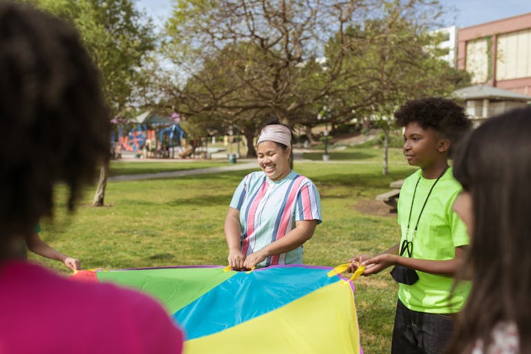 Happy kids enjoying outdoor activities with a colorful parachute at a summer camp.