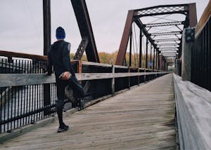 Man stretching on a wooden footbridge during a daytime run on an iron bridge, emphasizing fitness and recreation.