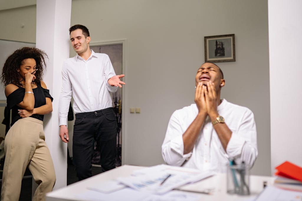 Three colleagues in an office setting display emotions of bullying and distress.