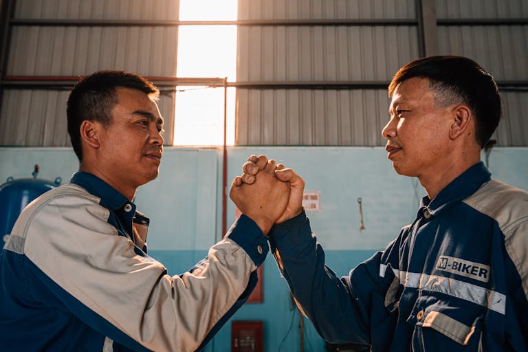 Two mechanics shaking hands in a sunlit workshop, symbolizing teamwork and unity.