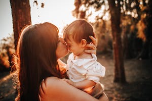 A mother and child sharing a loving embrace and kiss under warm sunlight.