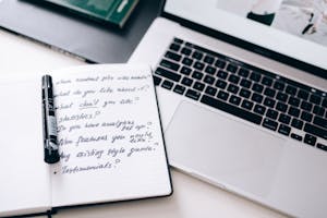 A notebook with handwritten notes next to a laptop on a workspace desk.