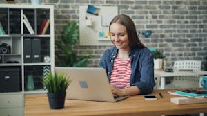 A woman uses a laptop at a stylish desk in a bright, modern office setting.