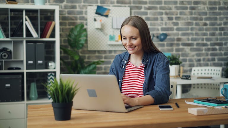 A woman uses a laptop at a stylish desk in a bright, modern office setting.