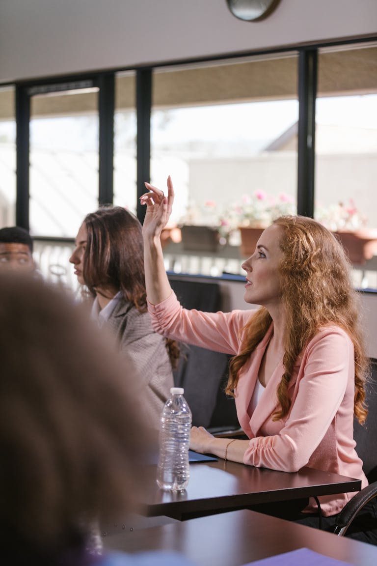 Red-haired woman actively participating in a business meeting, raising hand for discussion.