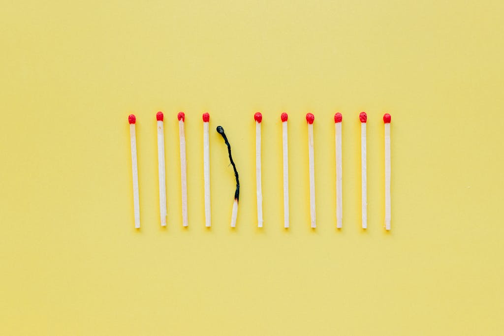 A burnt matchstick among unlit ones symbolizes burnout on a yellow background.