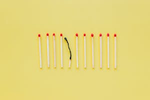 A burnt matchstick among unlit ones symbolizes burnout on a yellow background.