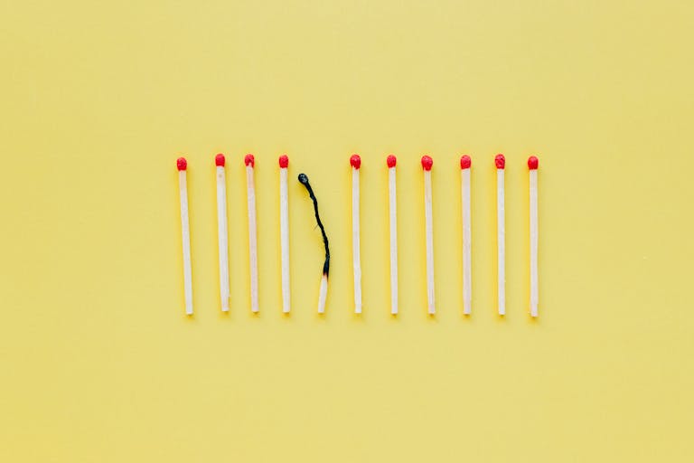 A burnt matchstick among unlit ones symbolizes burnout on a yellow background.